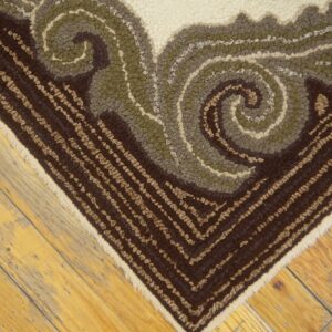 Textured brown, olive, and cream rug corner featuring a bold scroll pattern on light hardwood planks.