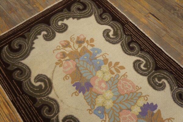 Detailed view of a cream rug featuring pastel florals and an olive green scrolled border on rustic wood planks.