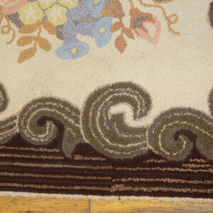 A highly textured rug displays pastel floral motifs on a cream field, bordered by dark brown and olive green scrolls.