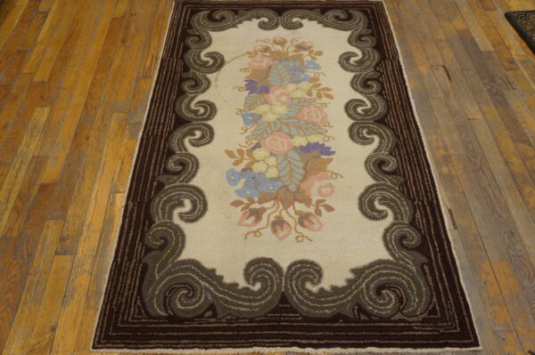 Floral hooked rug with a cream field and dark brown scrolling border on rustic wood planks.
