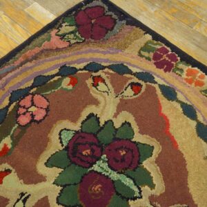 A close-up of a hooked rug showing burgundy and pink flowers, multicolor bands, and dark trim on wood flooring.
