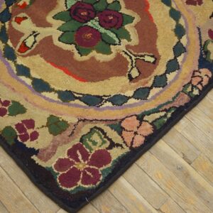 A corner of a textured floral rug with burgundy and tan colors rests on light wood planks.