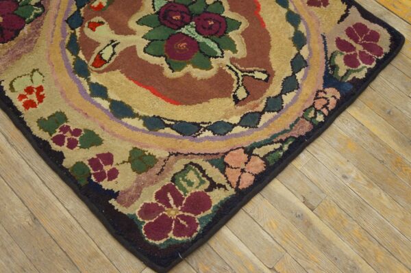 A corner of a textured floral rug with burgundy and tan colors rests on light wood planks.