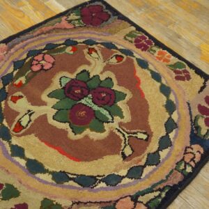 Textured rug featuring a central burgundy floral design and multi-colored concentric borders on wood planks.