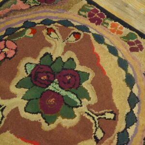 Earthy hooked rug with a rustic multicolored floral design featuring pink, burgundy, and green on wood floors.