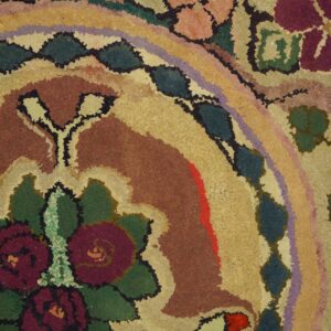 Textured loop rug featuring a bold floral design in rust, gold, burgundy, green, and purple on plank flooring.
