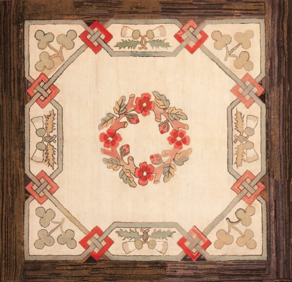 Square rug with a cream center, red floral wreath, framed by gray and red knots, surrounded by a dark brown border.