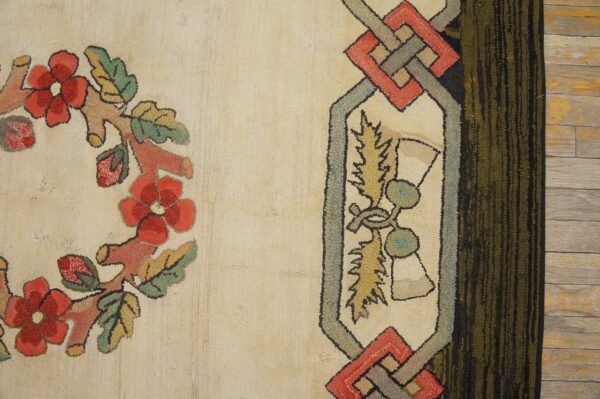 A textured loop rug displays a red floral wreath and geometric border against a cream field on wood flooring.