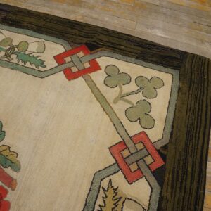 A richly textured rug corner displays red flowers, geometric shapes, and a dark striped border on wood floorboards.