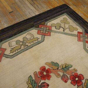 Beige textural rug corner displaying red floral motifs and interlocking borders against aged wood flooring.