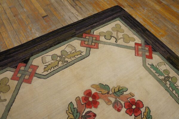 Beige textural rug corner displaying red floral motifs and interlocking borders against aged wood flooring.
