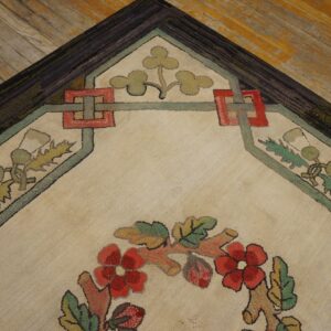 A textured cream rug with floral and geometric patterns in red, green, and brown lies on distressed wood flooring.