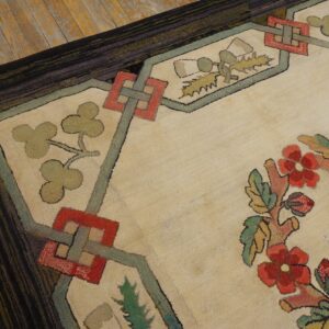 A textured cream rug with red and green floral and geometric patterns lies on worn wooden flooring.