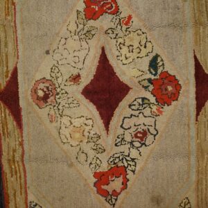 Textured rug featuring a large burgundy diamond and red floral motifs on a beige background over wood floorboards.