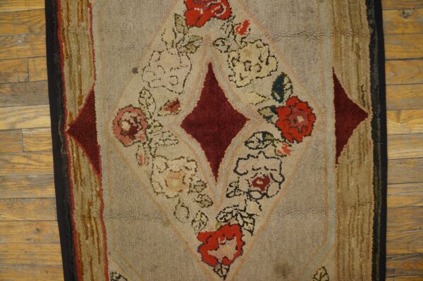 Textured rug featuring a large burgundy diamond and red floral motifs on a beige background over wood floorboards.