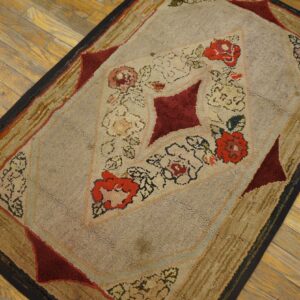 Textured beige and tan rug with a maroon and red floral diamond pattern on golden hardwood flooring.