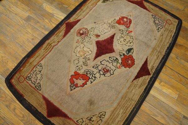 Textured beige and tan rug with a maroon and red floral diamond pattern on golden hardwood flooring.