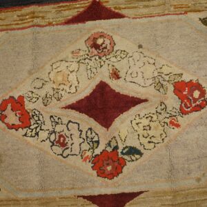 A textured rug displaying a central diamond pattern with red, pink, and cream floral designs on a light gray field.