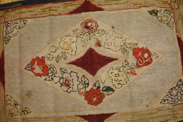 A textured rug displaying a central diamond pattern with red, pink, and cream floral designs on a light gray field.