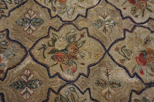 Heavily textured tan rug with dark blue ogee lattice framing muted red, cream, and green floral details.