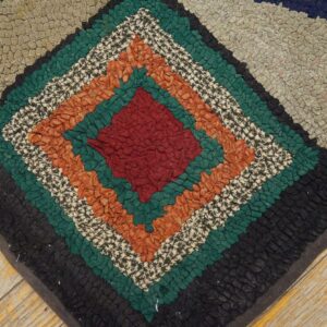 Textured rag rug with concentric diamonds in red, green, orange, and black on worn wood floor.