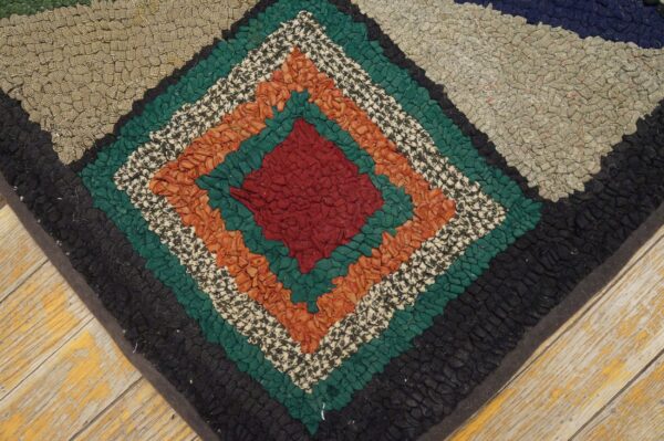Textured rag rug with concentric diamonds in red, green, orange, and black on worn wood floor.