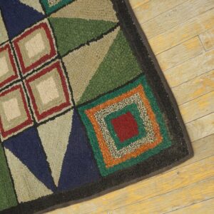 A multi-colored geometric hooked rug with squares and triangles rests on distressed yellow wood floorboards.
