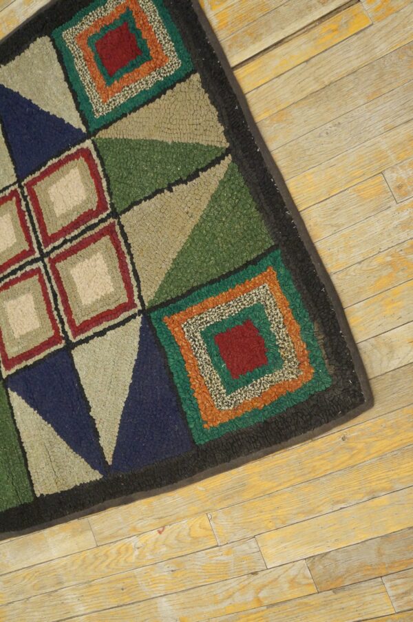 A multi-colored geometric hooked rug with squares and triangles rests on distressed yellow wood floorboards.