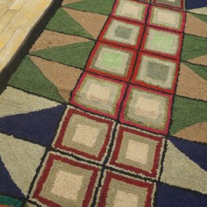 Geometric textured runner rug featuring concentric squares and triangles on yellow wood planks.