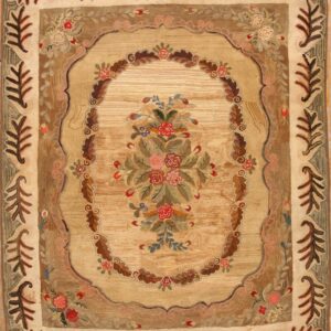 Tan and brown textured rug with a central multi-colored floral bouquet and wide borders of large stylized leaves.