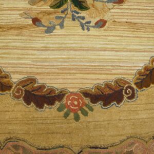 A looped tan and gold rug detailed with a scrolling border of brown leaves and red floral motifs.