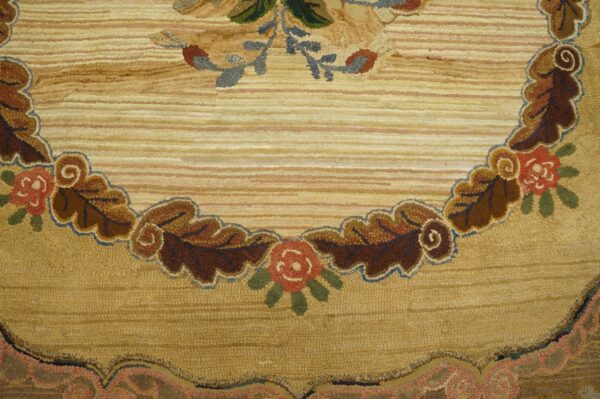 A looped tan and gold rug detailed with a scrolling border of brown leaves and red floral motifs.