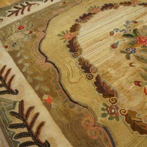 Sculpted, antique-style rug in tan, gold, brown, and red, featuring elaborate floral borders over wood planks.