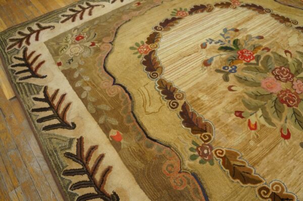 Sculpted, antique-style rug in tan, gold, brown, and red, featuring elaborate floral borders over wood planks.