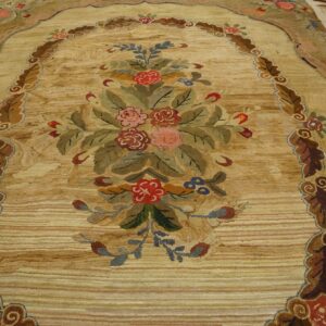 Detailed view of a textured beige rug with an arched, colorful floral bouquet and carved leaf borders.