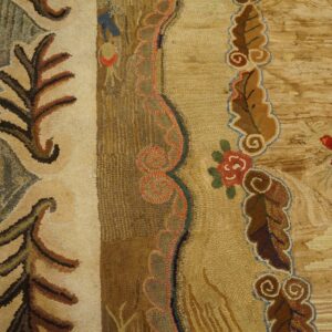 Textured, multi-colored hooked rug with bold floral borders lies next to distressed plank wood flooring.