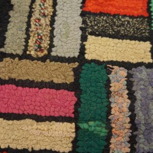 Colorful patchwork rug features dense, textured loops of pink, green, orange, and mixed shades against a dark ground.