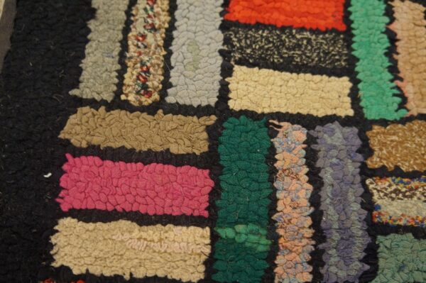 Colorful patchwork rug features dense, textured loops of pink, green, orange, and mixed shades against a dark ground.