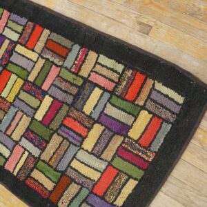 Colorful hooked rug runner featuring a herringbone block pattern and dark border on distressed wood flooring.