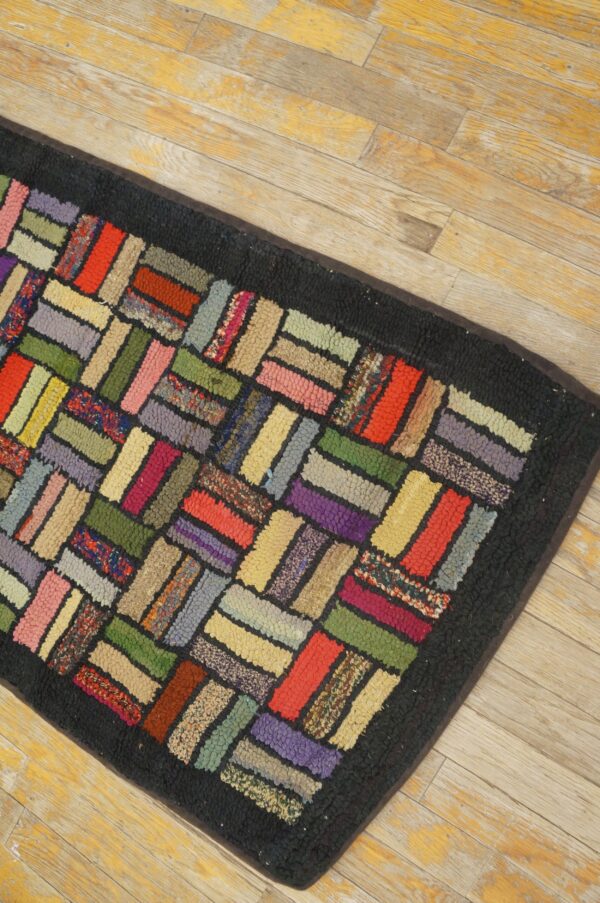 Colorful hooked rug runner featuring a herringbone block pattern and dark border on distressed wood flooring.