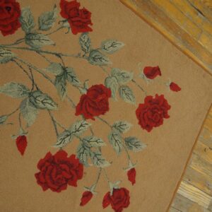 A tan shag rug featuring a red and pale green rose floral pattern rests on rustic yellow wood plank flooring.