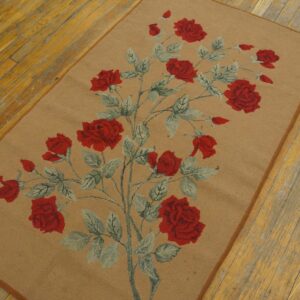Low-pile tan rug featuring red roses and sage leaves rests on distressed yellow wood flooring.