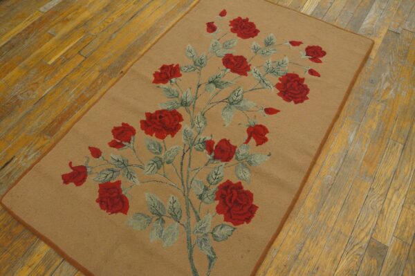 Low-pile tan rug featuring red roses and sage leaves rests on distressed yellow wood flooring.