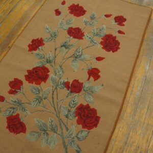 Looped rug with a tan field and red rose vine pattern rests on distressed yellow wood floorboards.