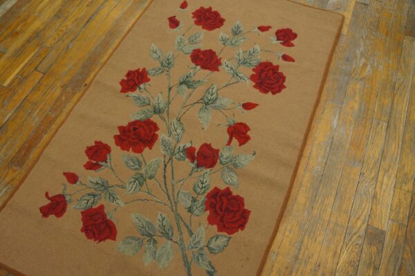 Looped rug with a tan field and red rose vine pattern rests on distressed yellow wood floorboards.
