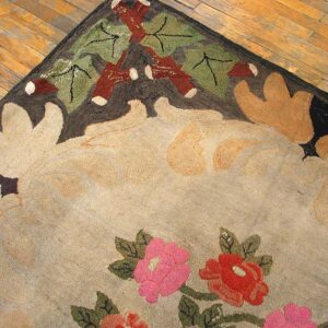 Beige rug with large floral pattern, pink and red blooms, and dark brown border on wood planks.