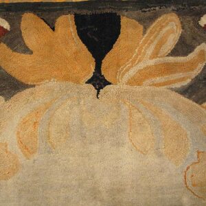 Close-up of a hooked floral rug with scalloped motifs in cream, gold, green, and dark brown.