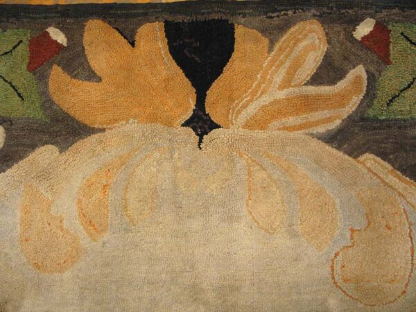 Close-up of a hooked floral rug with scalloped motifs in cream, gold, green, and dark brown.