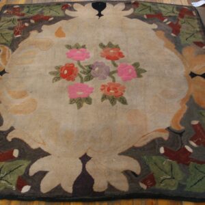 Beige rug with pink and red floral centerpiece and dark brown stylized border lying on wood planks.