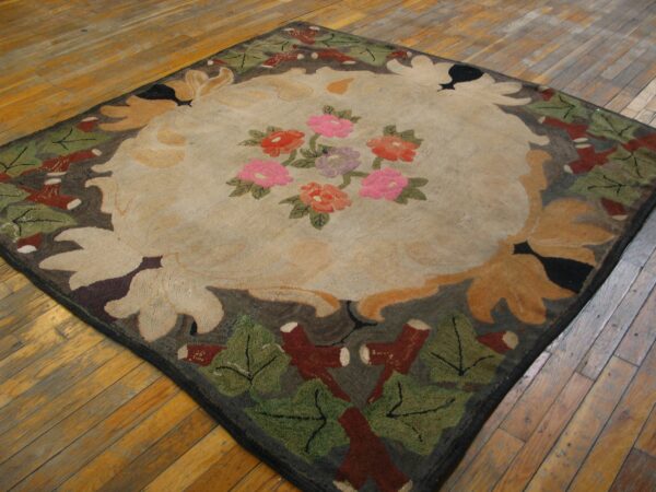 Square rug with a beige center, pink and red flowers, and a dark leaf border on plank hardwood.